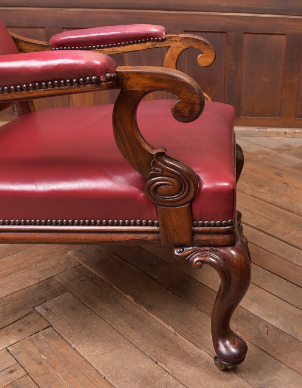 A Regency period rosewood armchair featuring dark red button-tufted leather upholstery, scrolled armrests, brass castors, and carved timber detailing. View XXV