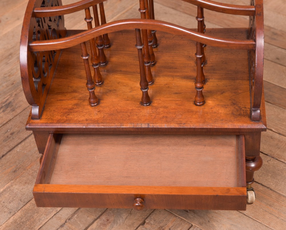A Victorian walnut Canterbury featuring carved fretwork side panels, turned spindle dividers, a single lower drawer, and turned legs with brass castors. View II