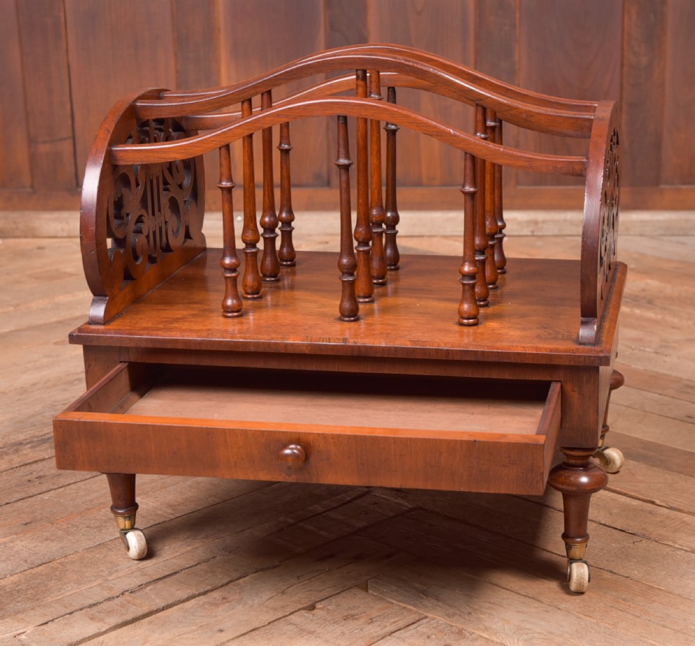 A Victorian walnut Canterbury featuring carved fretwork side panels, turned spindle dividers, a single lower drawer, and turned legs with brass castors. View III