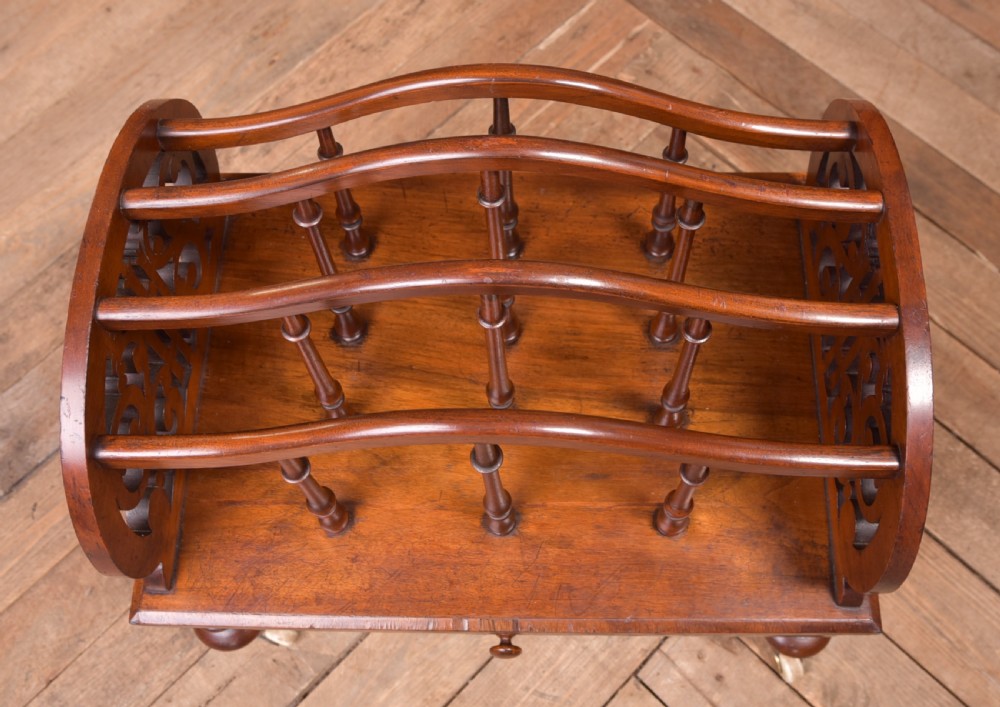 A Victorian walnut Canterbury featuring carved fretwork side panels, turned spindle dividers, a single lower drawer, and turned legs with brass castors. View VIII