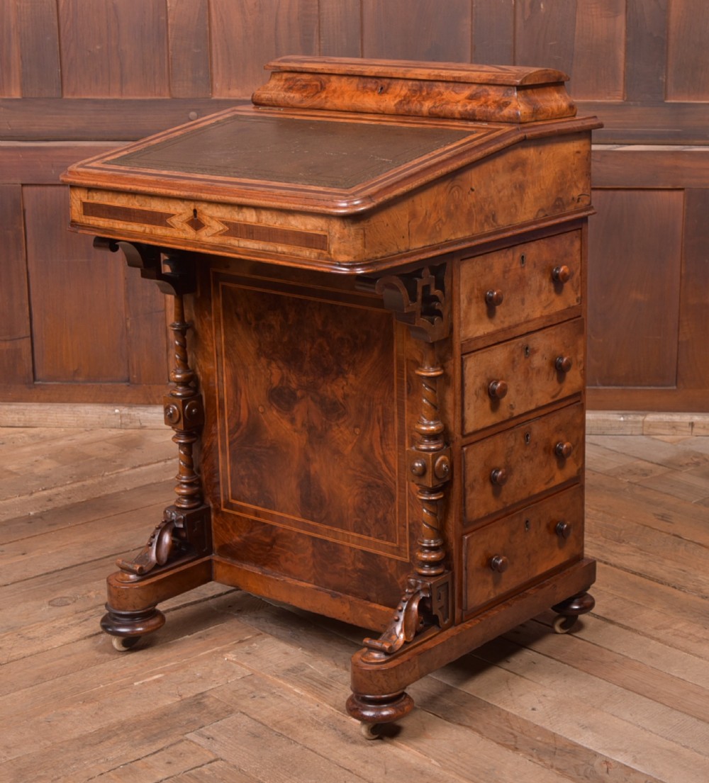 A Victorian burr walnut Davenport desk featuring a slanted leather writing surface, decorative carved supports, and a side bank of drawers.