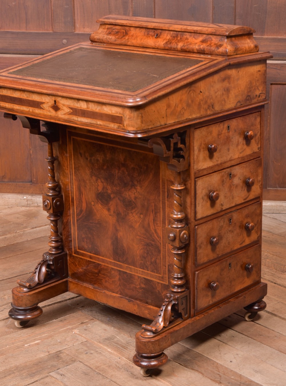 A Victorian burr walnut Davenport desk featuring a slanted leather writing surface, decorative carved supports, and a side bank of drawers. View V