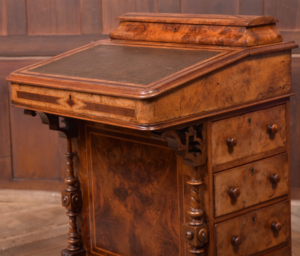A Victorian burr walnut Davenport desk featuring a slanted leather writing surface, decorative carved supports, and a side bank of drawers. View VI