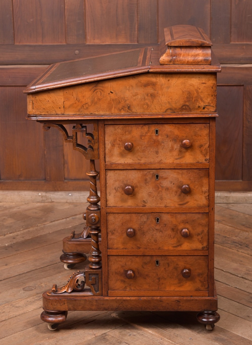 A Victorian burr walnut Davenport desk featuring a slanted leather writing surface, decorative carved supports, and a side bank of drawers. View VII