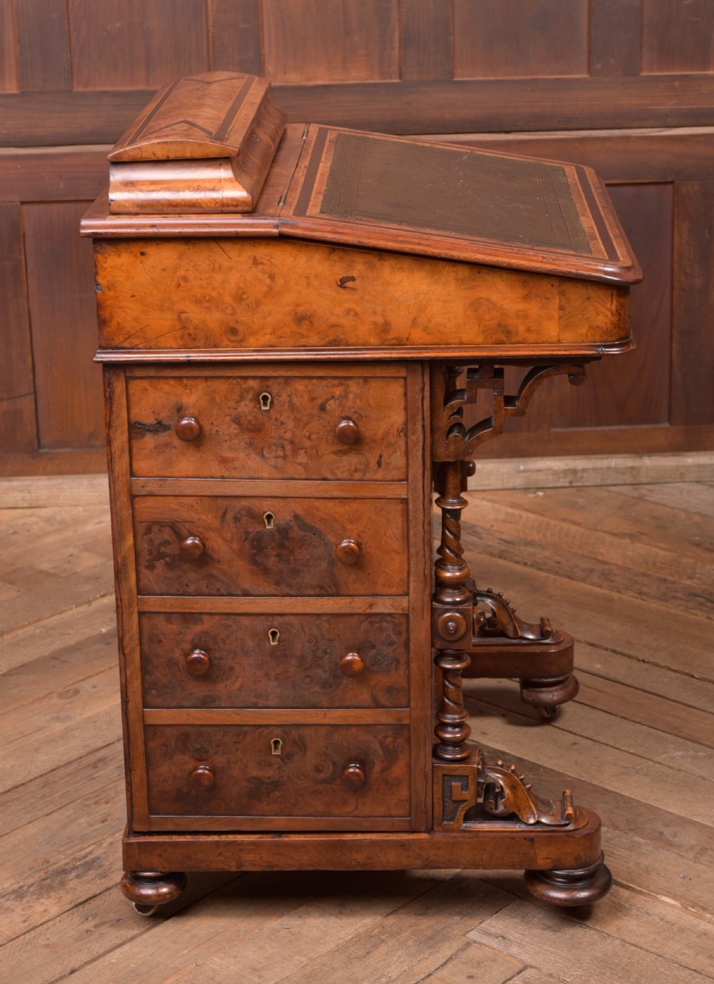 A Victorian burr walnut Davenport desk featuring a slanted leather writing surface, decorative carved supports, and a side bank of drawers. View X