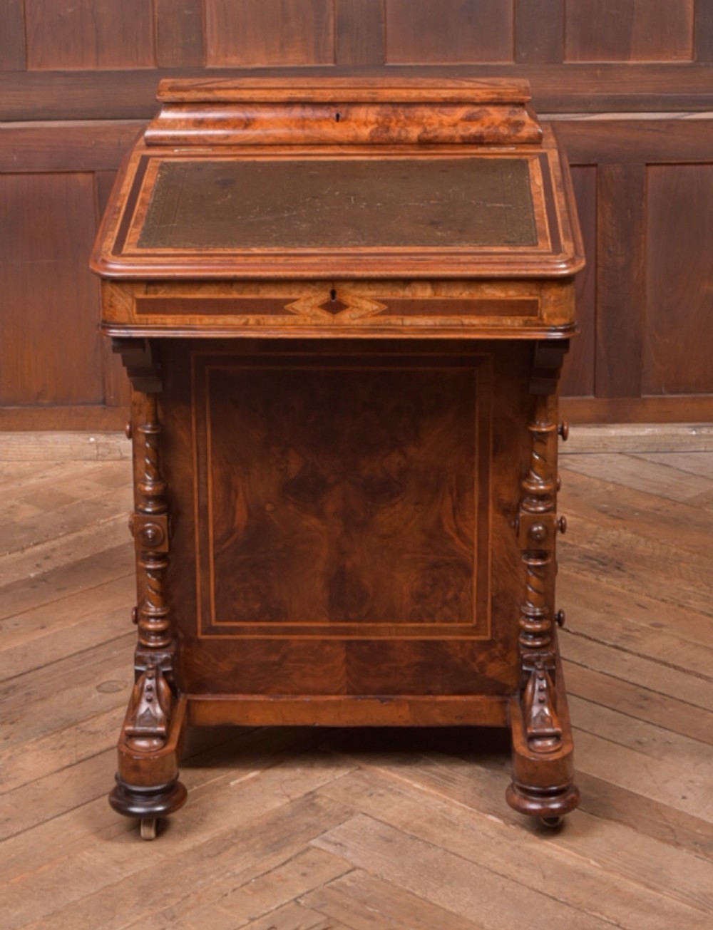 A Victorian burr walnut Davenport desk featuring a slanted leather writing surface, decorative carved supports, and a side bank of drawers. View XV