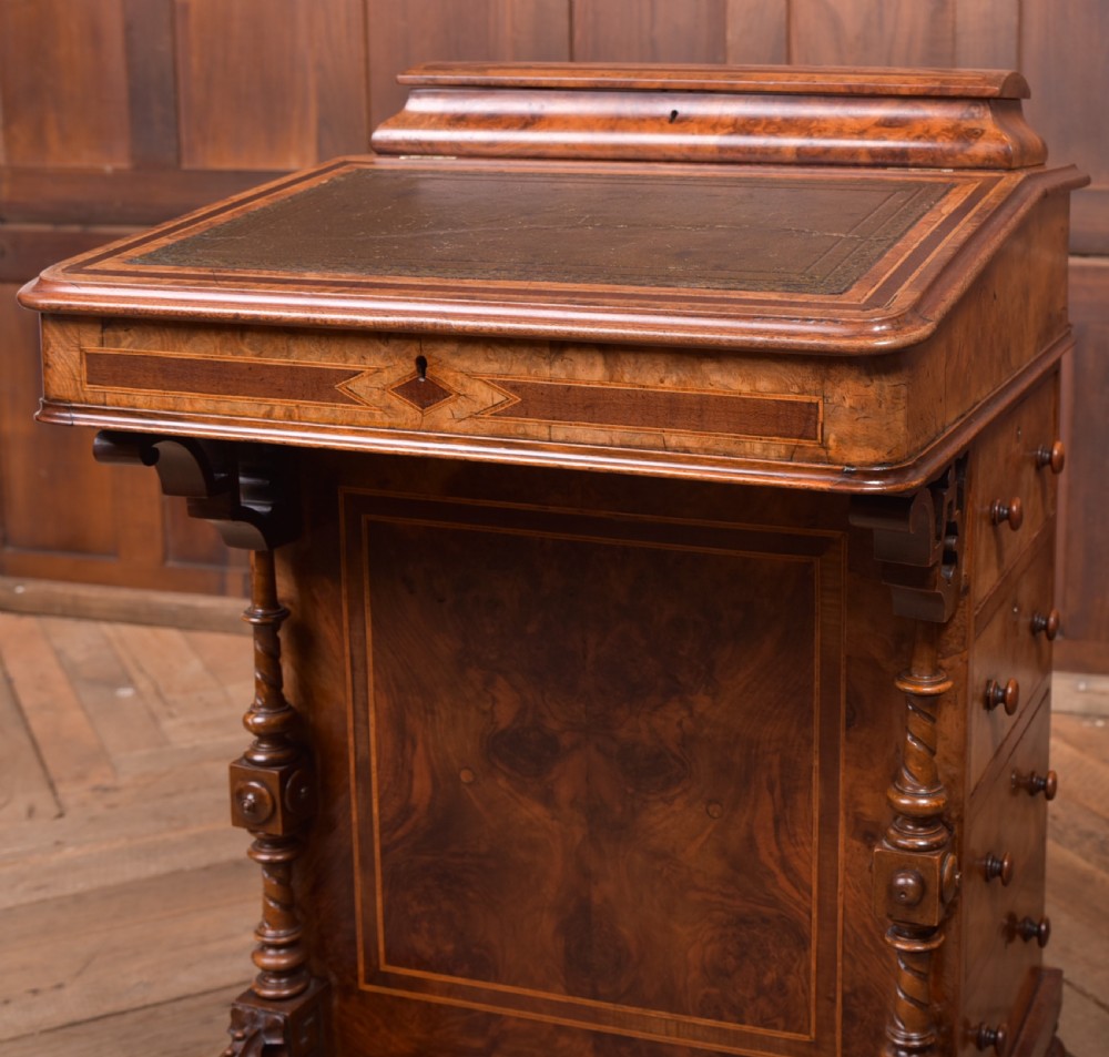 A Victorian burr walnut Davenport desk featuring a slanted leather writing surface, decorative carved supports, and a side bank of drawers. View XVII