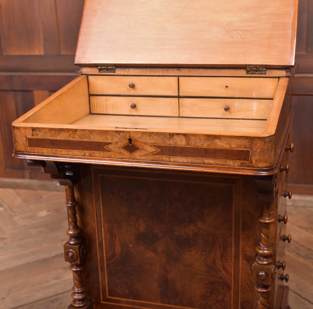 A Victorian burr walnut Davenport desk featuring a slanted leather writing surface, decorative carved supports, and a side bank of drawers. View XIX