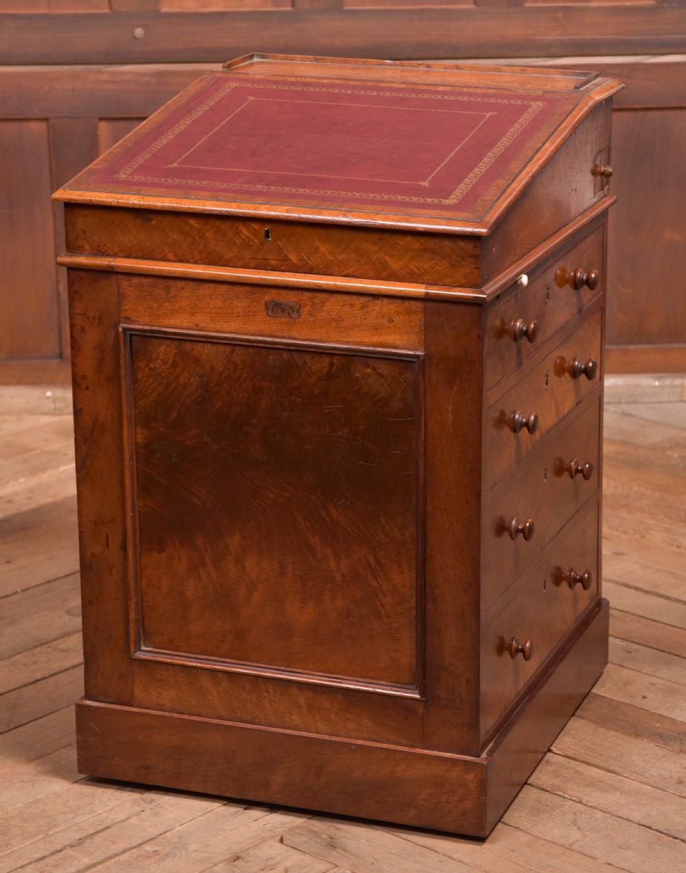 A Victorian walnut Davenport desk featuring a slanted burgundy leather writing surface, side drawers with wooden knobs, and a solid rectangular base.