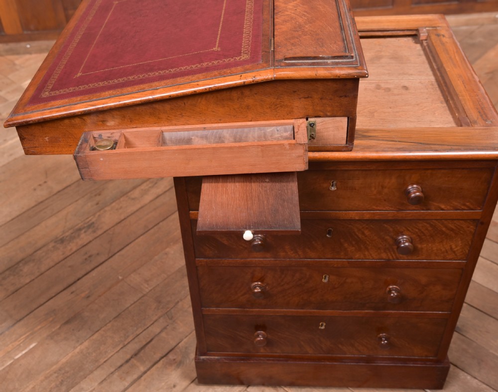 A Victorian walnut Davenport desk featuring a slanted burgundy leather writing surface, side drawers with wooden knobs, and a solid rectangular base. View VI