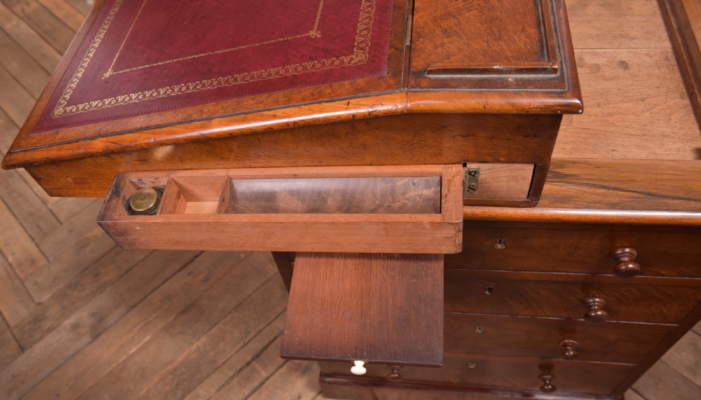 A Victorian walnut Davenport desk featuring a slanted burgundy leather writing surface, side drawers with wooden knobs, and a solid rectangular base. View VII