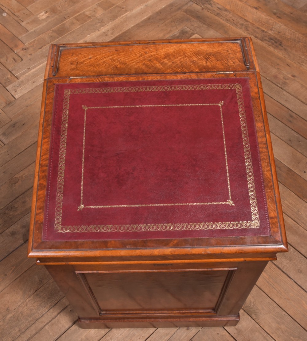 A Victorian walnut Davenport desk featuring a slanted burgundy leather writing surface, side drawers with wooden knobs, and a solid rectangular base. View XIX