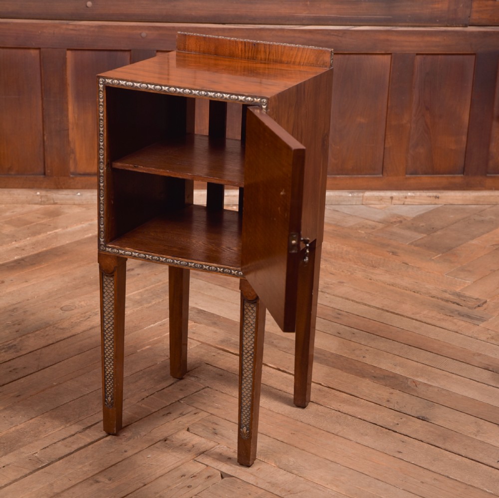 An antique walnut bedside cabinet featuring a single door panel with burr walnut veneer, beaded metal trim, a top splashback upstand, and four square tapered legs. View II