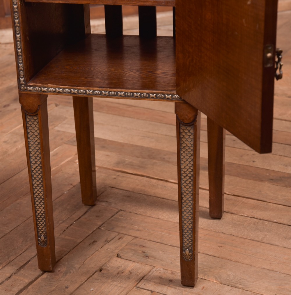 An antique walnut bedside cabinet featuring a single door panel with burr walnut veneer, beaded metal trim, a top splashback upstand, and four square tapered legs. View V