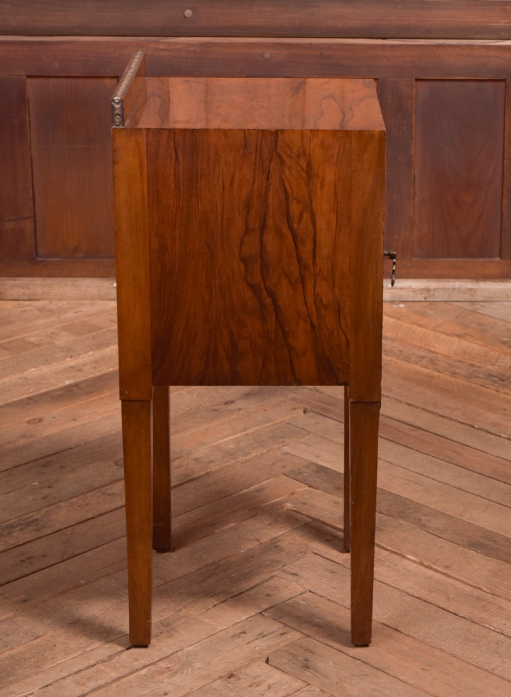 An antique walnut bedside cabinet featuring a single door panel with burr walnut veneer, beaded metal trim, a top splashback upstand, and four square tapered legs. View IX
