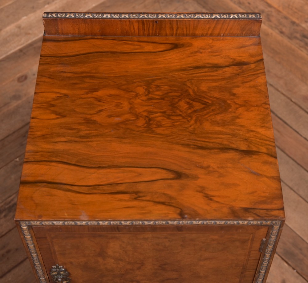 An antique walnut bedside cabinet featuring a single door panel with burr walnut veneer, beaded metal trim, a top splashback upstand, and four square tapered legs. View X