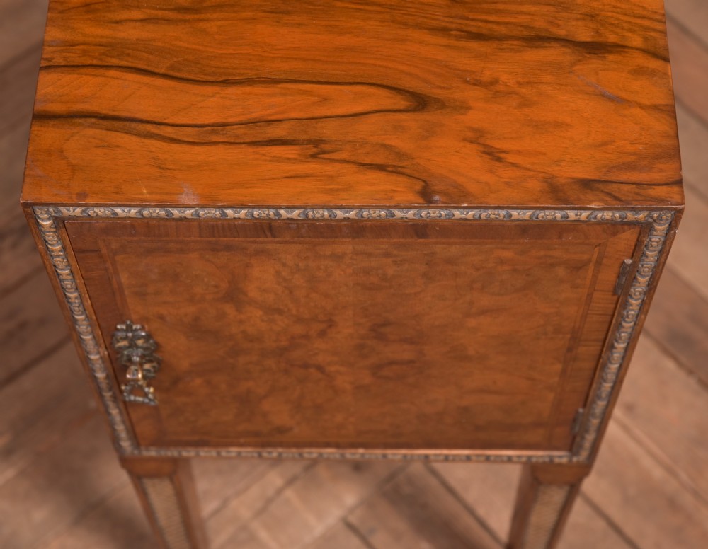 An antique walnut bedside cabinet featuring a single door panel with burr walnut veneer, beaded metal trim, a top splashback upstand, and four square tapered legs. View XI