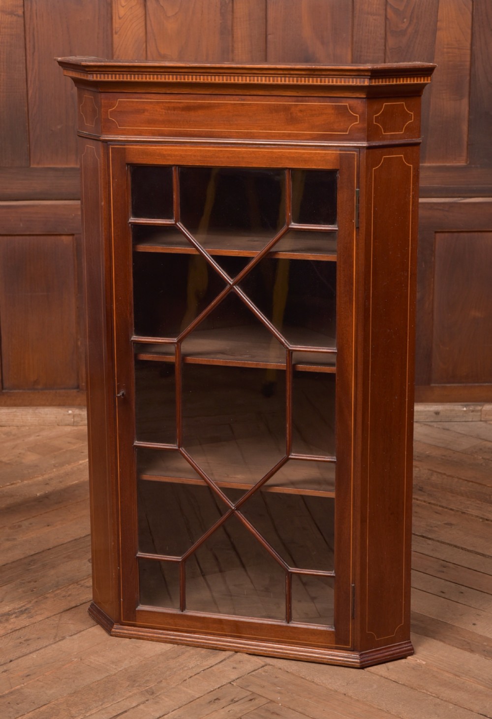 An Edwardian mahogany corner cabinet featuring astragal glazed glass panels, geometric boxwood line inlay, and internal timber shelves.