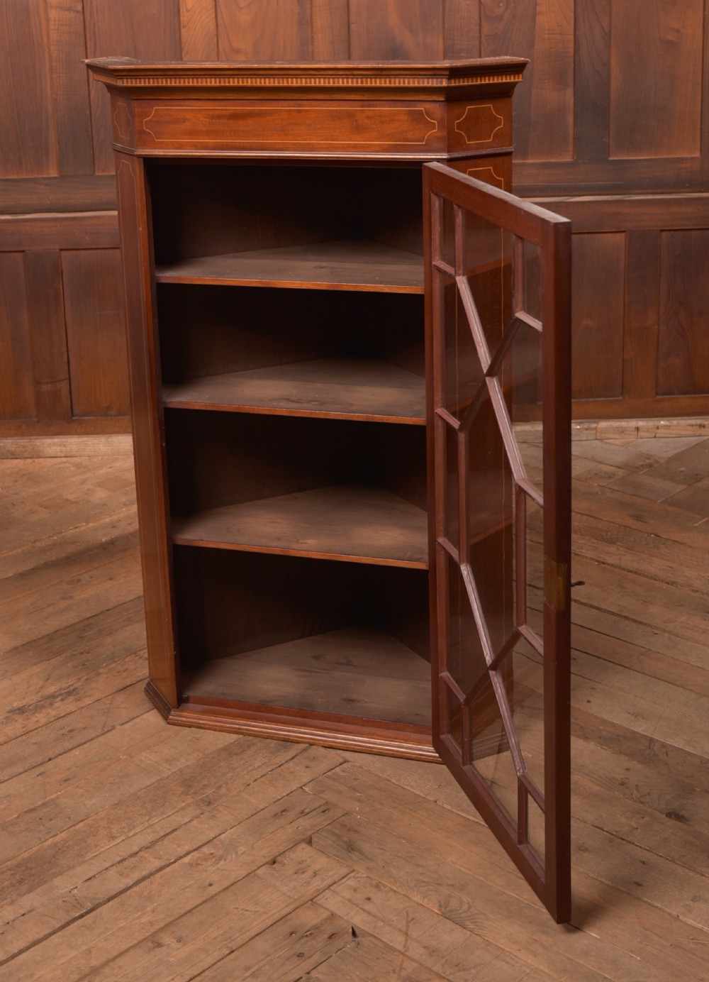 An Edwardian mahogany corner cabinet featuring astragal glazed glass panels, geometric boxwood line inlay, and internal timber shelves. View VII