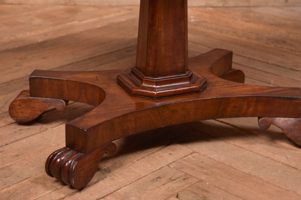 A Victorian mahogany card table featuring a rectangular fold-over top set upon a central tapered pedestal and a quadripartite plinth base with carved feet. View III