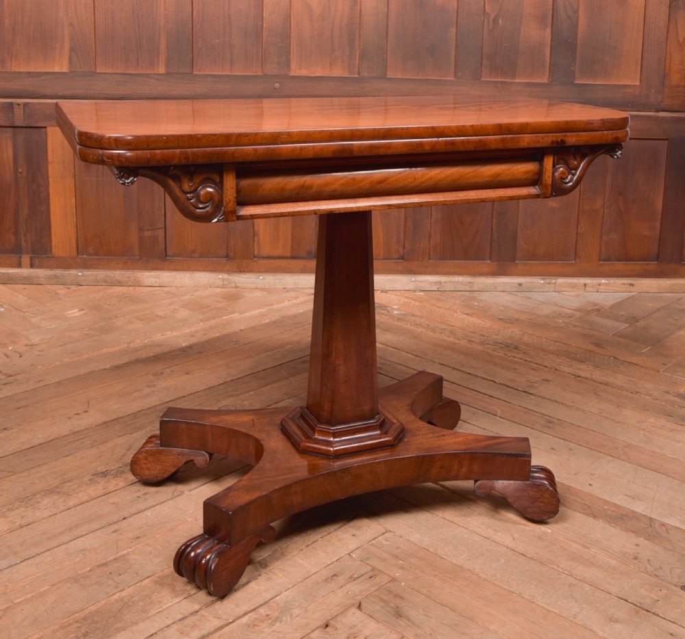 A Victorian mahogany card table featuring a rectangular fold-over top set upon a central tapered pedestal and a quadripartite plinth base with carved feet. View VII