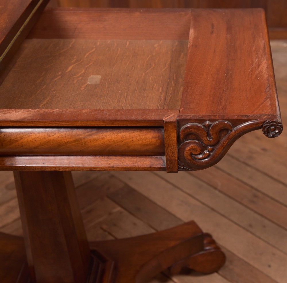 A Victorian mahogany card table featuring a rectangular fold-over top set upon a central tapered pedestal and a quadripartite plinth base with carved feet. View X