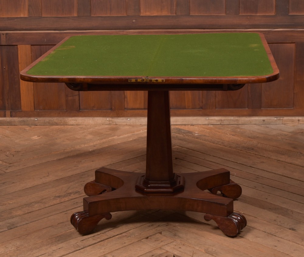 A Victorian mahogany card table featuring a rectangular fold-over top set upon a central tapered pedestal and a quadripartite plinth base with carved feet. View XI