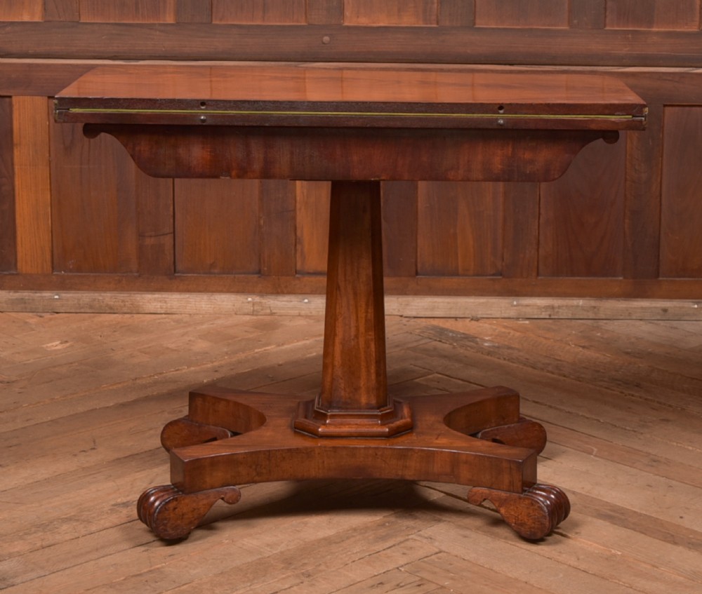 A Victorian mahogany card table featuring a rectangular fold-over top set upon a central tapered pedestal and a quadripartite plinth base with carved feet. View XIV