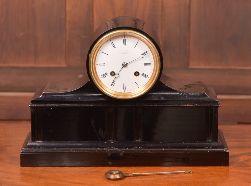 A Victorian black ebonised mantel clock featuring a circular brass-rimmed dial with Roman numerals set above a rectangular plinth base.