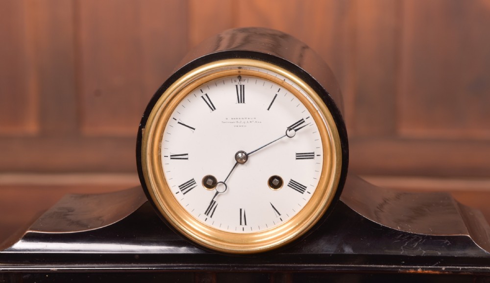 A Victorian black ebonised mantel clock featuring a circular brass-rimmed dial with Roman numerals set above a rectangular plinth base. View III
