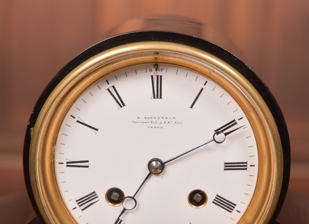 A Victorian black ebonised mantel clock featuring a circular brass-rimmed dial with Roman numerals set above a rectangular plinth base. View V