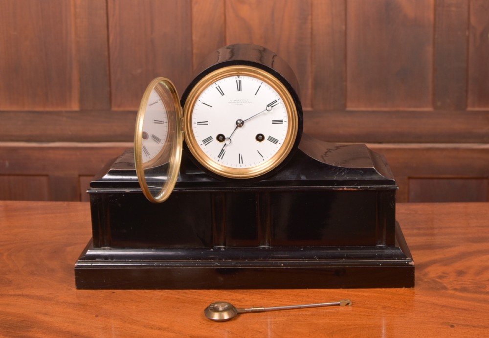 A Victorian black ebonised mantel clock featuring a circular brass-rimmed dial with Roman numerals set above a rectangular plinth base. View VI