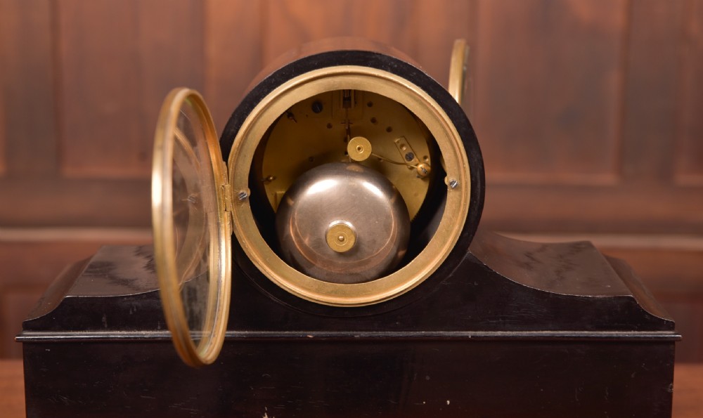 A Victorian black ebonised mantel clock featuring a circular brass-rimmed dial with Roman numerals set above a rectangular plinth base. View VIII