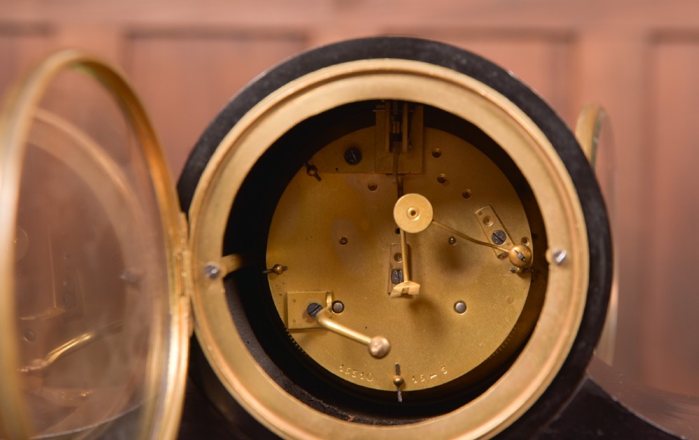 A Victorian black ebonised mantel clock featuring a circular brass-rimmed dial with Roman numerals set above a rectangular plinth base. View X