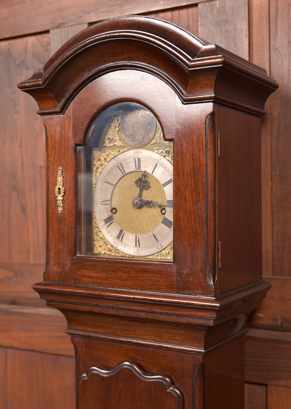 A freestanding mahogany grandmother clock featuring an arched hood, brass dial with corner spandrels, a slender waist door, and brass weights placed in front. View III