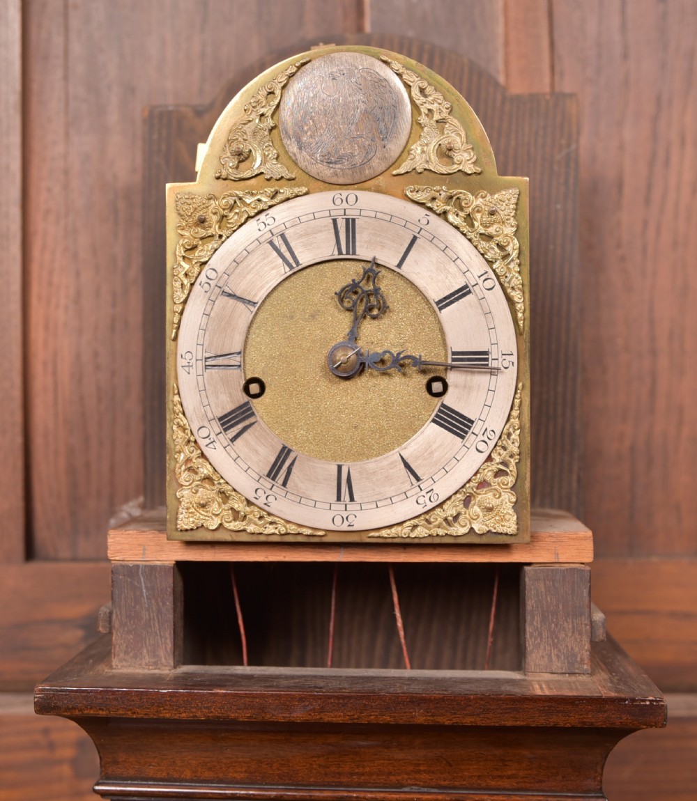A freestanding mahogany grandmother clock featuring an arched hood, brass dial with corner spandrels, a slender waist door, and brass weights placed in front. View VIII