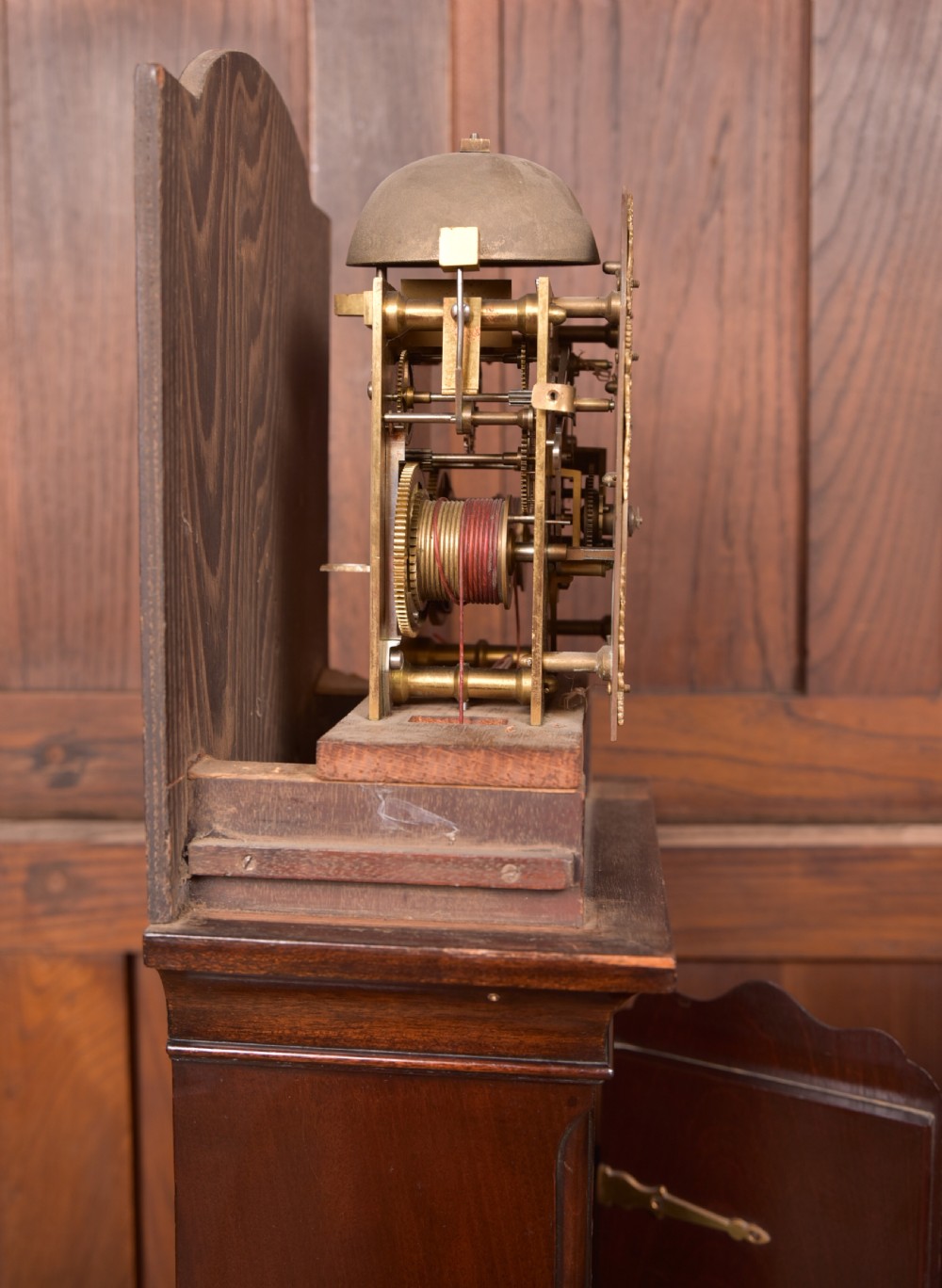 A freestanding mahogany grandmother clock featuring an arched hood, brass dial with corner spandrels, a slender waist door, and brass weights placed in front. View IX