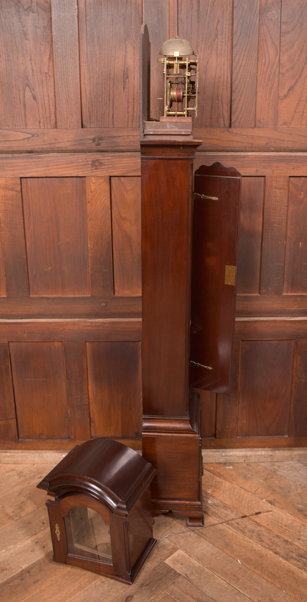A freestanding mahogany grandmother clock featuring an arched hood, brass dial with corner spandrels, a slender waist door, and brass weights placed in front. View X
