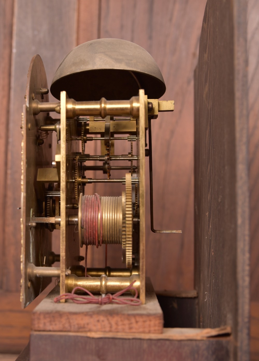 A freestanding mahogany grandmother clock featuring an arched hood, brass dial with corner spandrels, a slender waist door, and brass weights placed in front. View XII