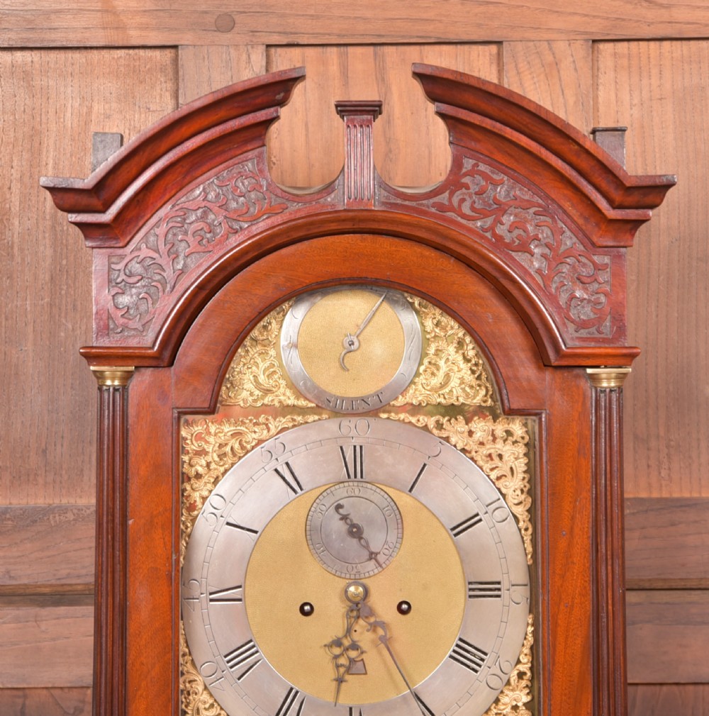 An antique Georgian flame mahogany longcase clock with a swan-neck pediment and an arched brass dial. View II