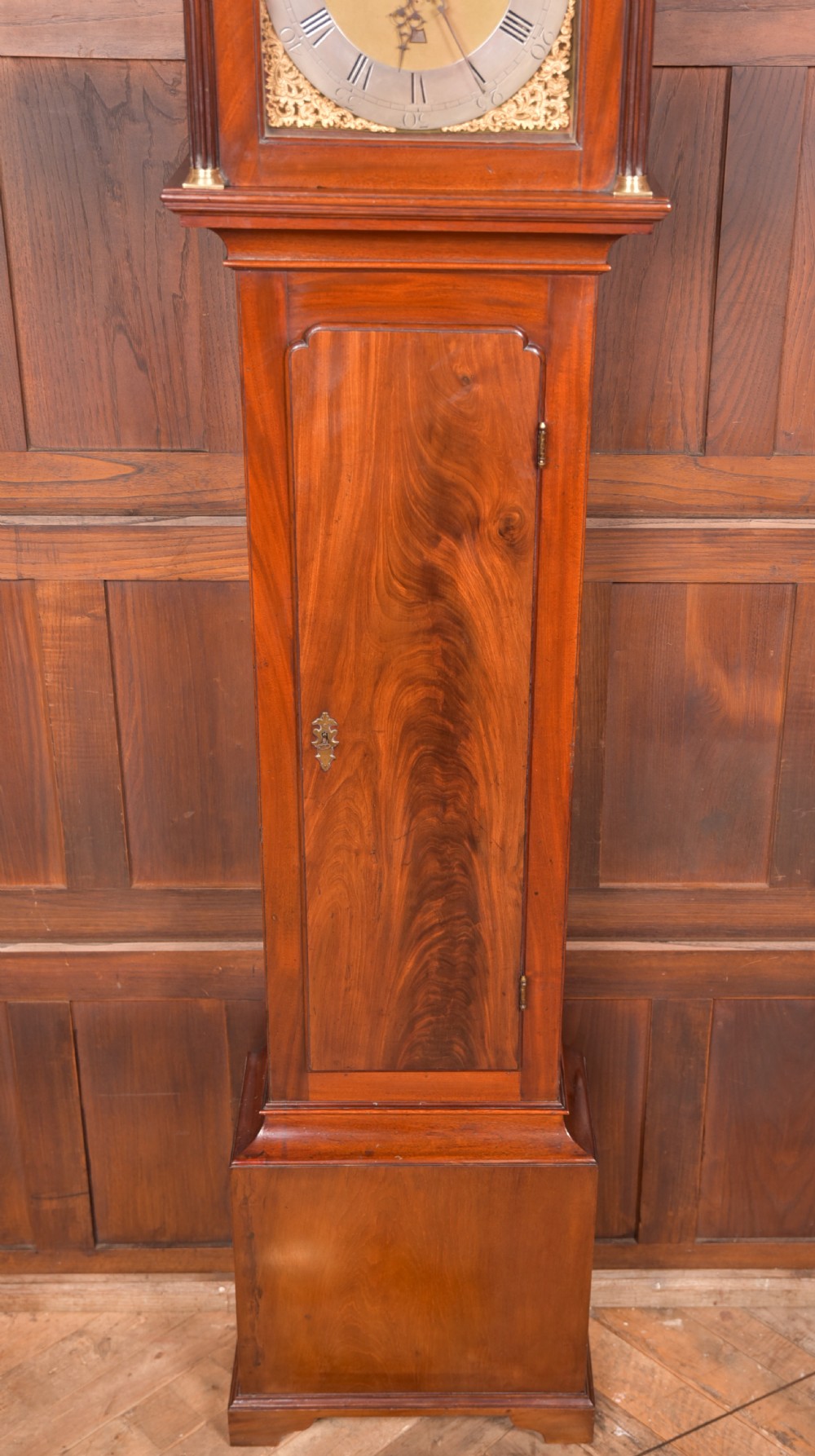 An antique Georgian flame mahogany longcase clock with a swan-neck pediment and an arched brass dial. View V