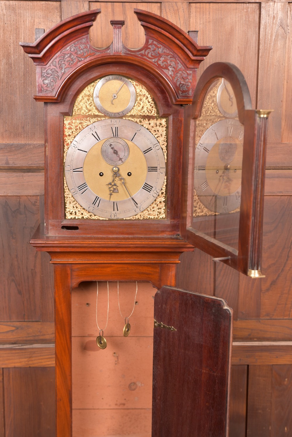 An antique Georgian flame mahogany longcase clock with a swan-neck pediment and an arched brass dial. View VIII