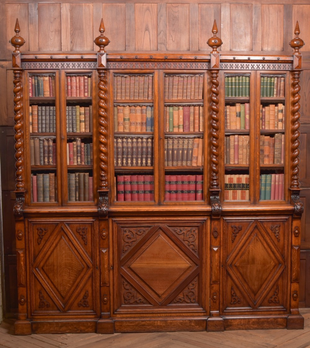 A large Victorian oak bookcase featuring glazed upper doors flanked by barley twist columns with turned finials above carved diamond panel doors.