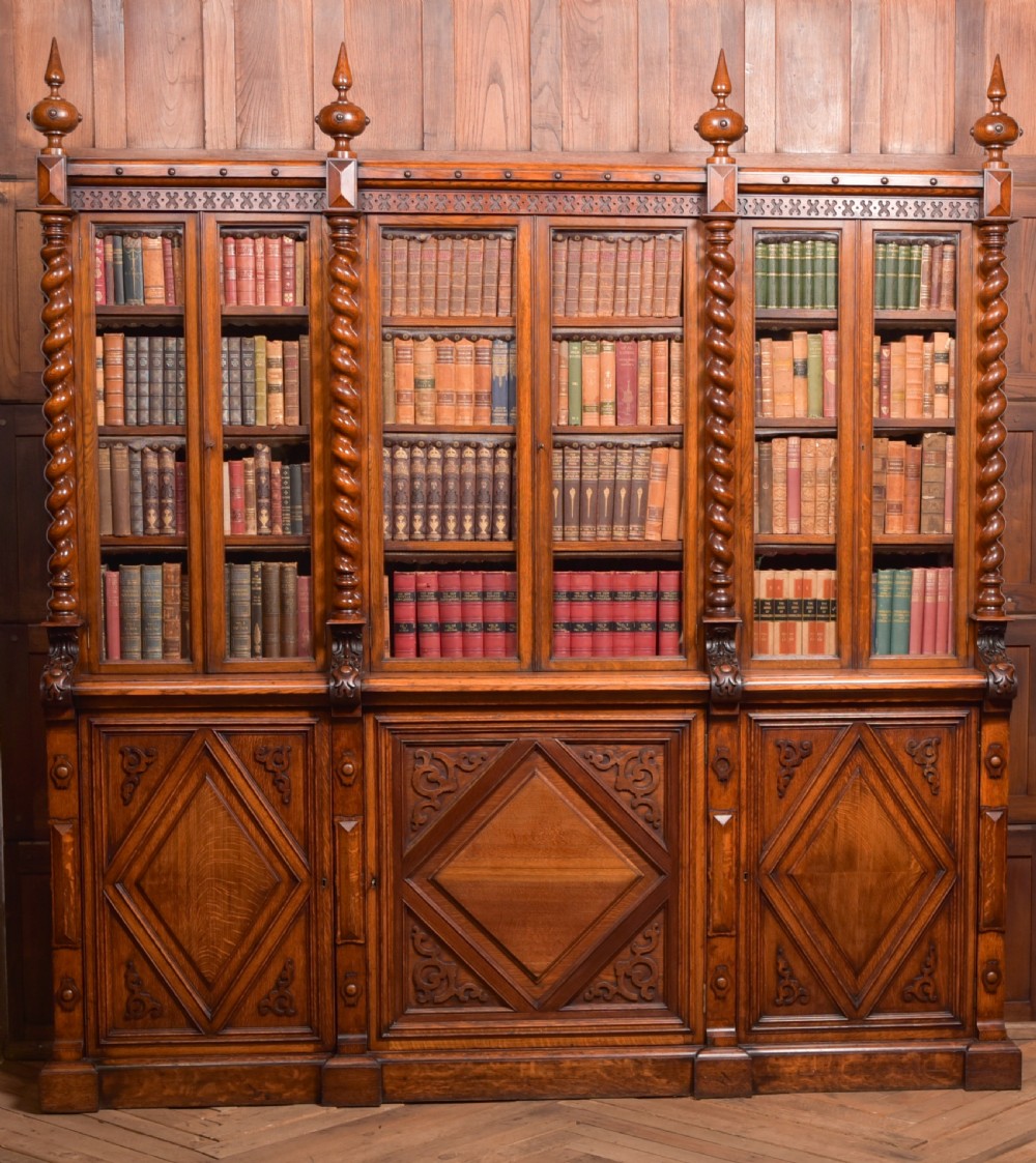 A large Victorian oak bookcase featuring glazed upper doors flanked by barley twist columns with turned finials above carved diamond panel doors. View II