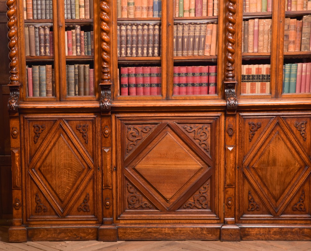 A large Victorian oak bookcase featuring glazed upper doors flanked by barley twist columns with turned finials above carved diamond panel doors. View VI