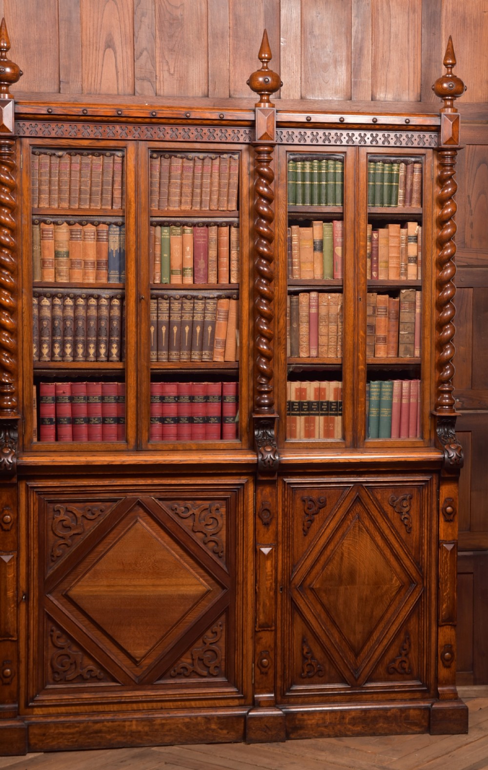 A large Victorian oak bookcase featuring glazed upper doors flanked by barley twist columns with turned finials above carved diamond panel doors. View VIII