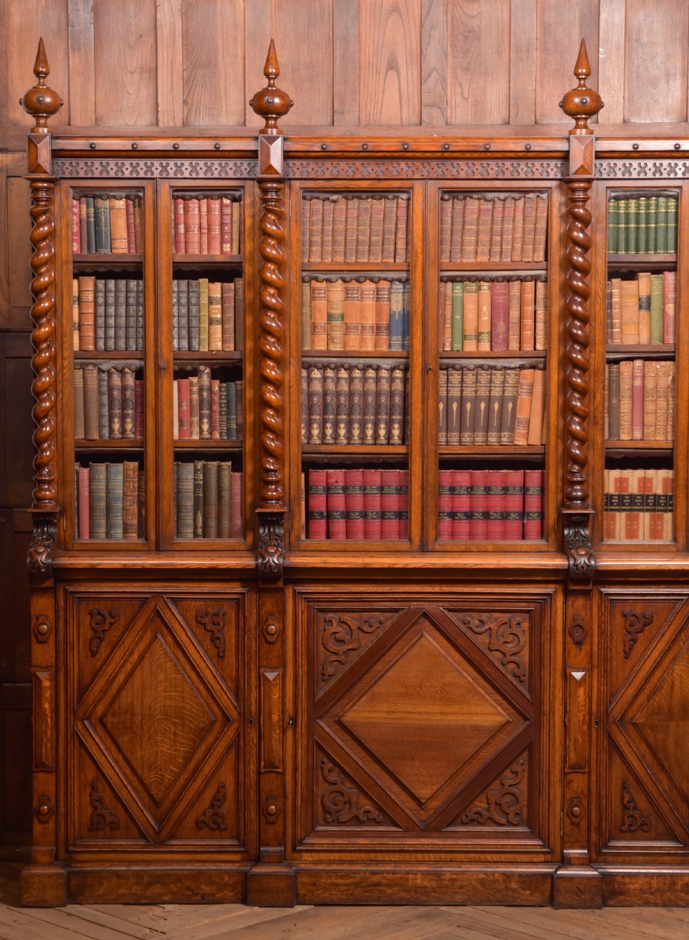 A large Victorian oak bookcase featuring glazed upper doors flanked by barley twist columns with turned finials above carved diamond panel doors. View IX