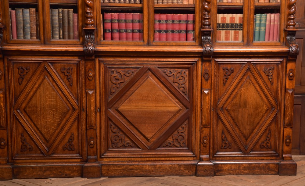 A large Victorian oak bookcase featuring glazed upper doors flanked by barley twist columns with turned finials above carved diamond panel doors. View XI