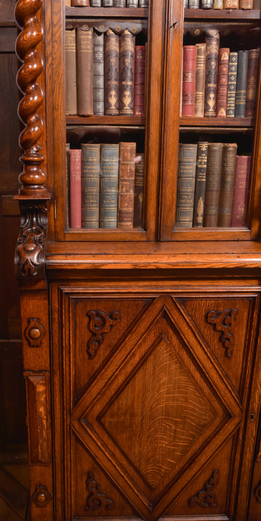 A large Victorian oak bookcase featuring glazed upper doors flanked by barley twist columns with turned finials above carved diamond panel doors. View XVI