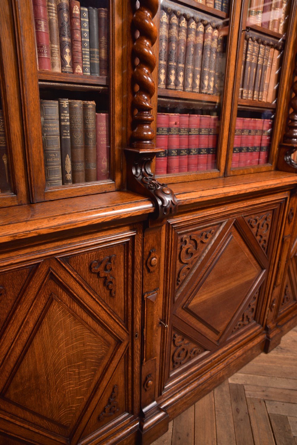 A large Victorian oak bookcase featuring glazed upper doors flanked by barley twist columns with turned finials above carved diamond panel doors. View XVII